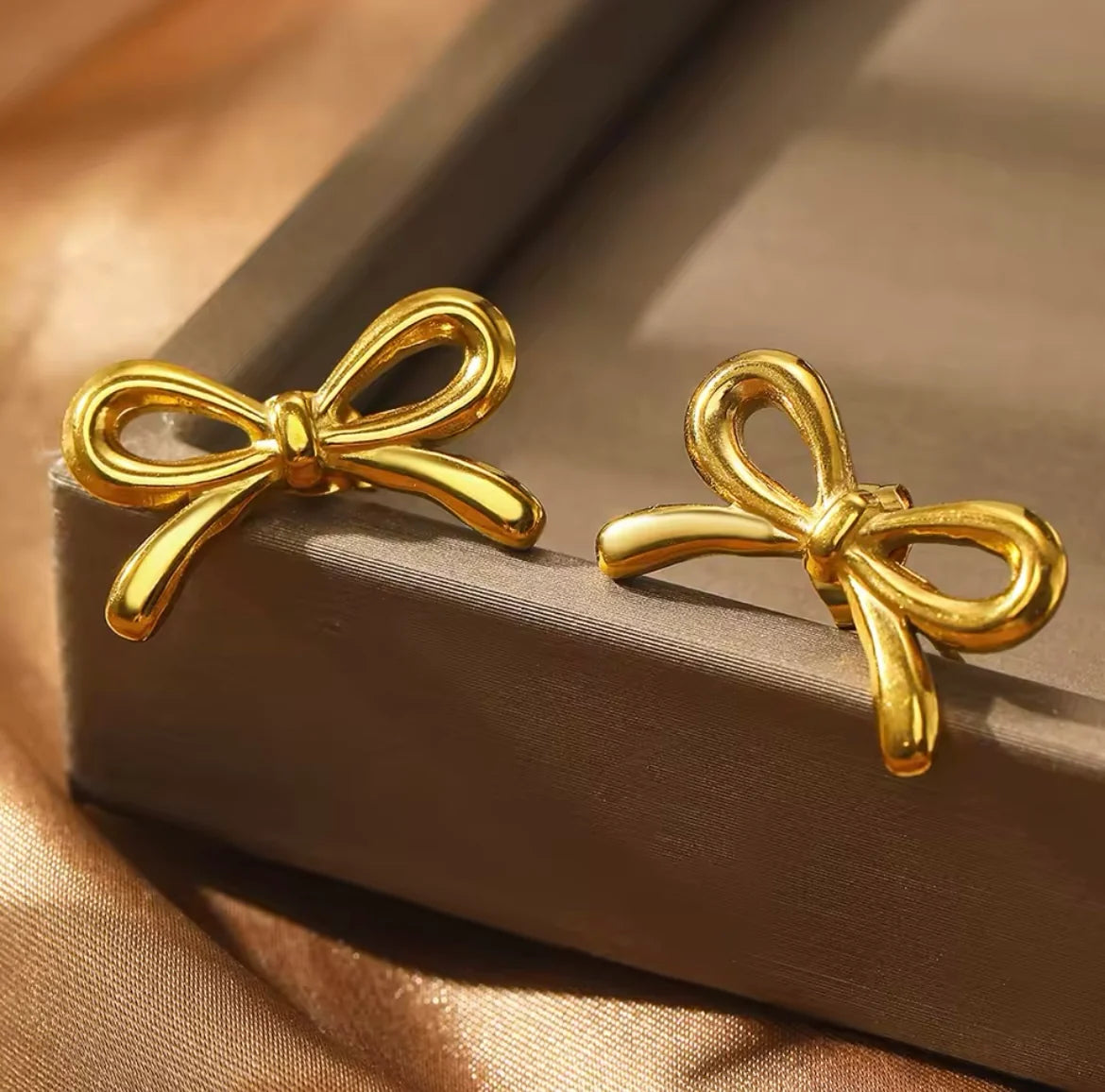 Gold bow stud earrings resting on grey book with bokeh background
