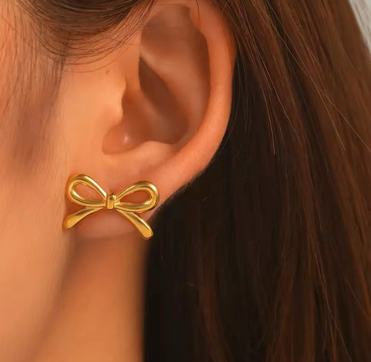 Gold bow stud earring worn on model ear close-up