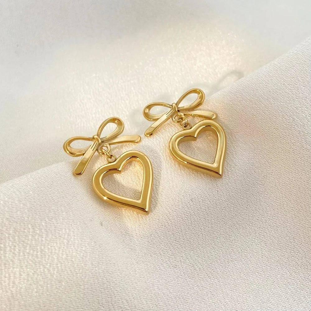Gold bow and open heart drop earrings on white linen fabric