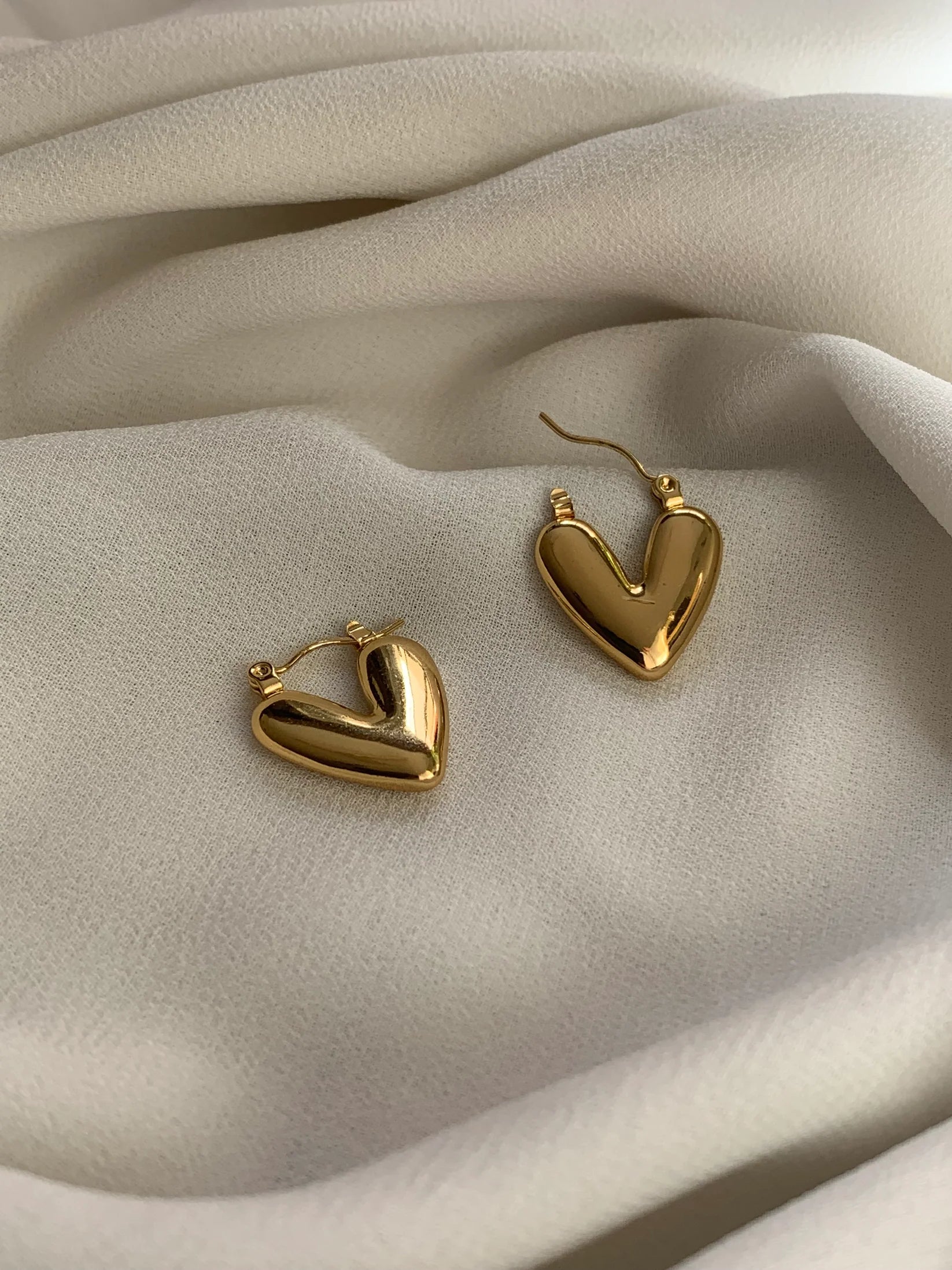 Gold puffy heart hoop earrings on linen fabric