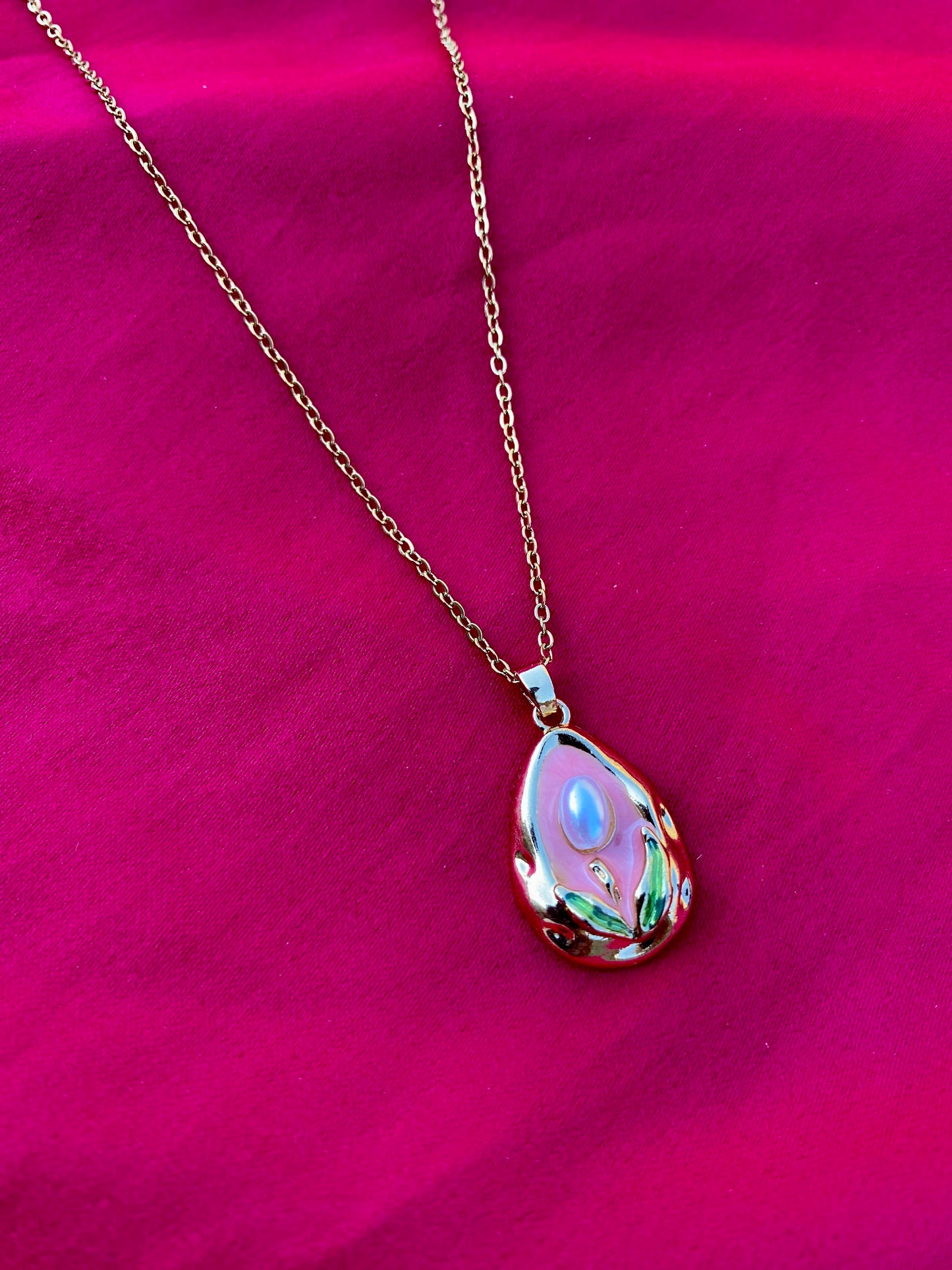 Modern Gold Drop Necklace with Pearl Detail on a Pink Background
