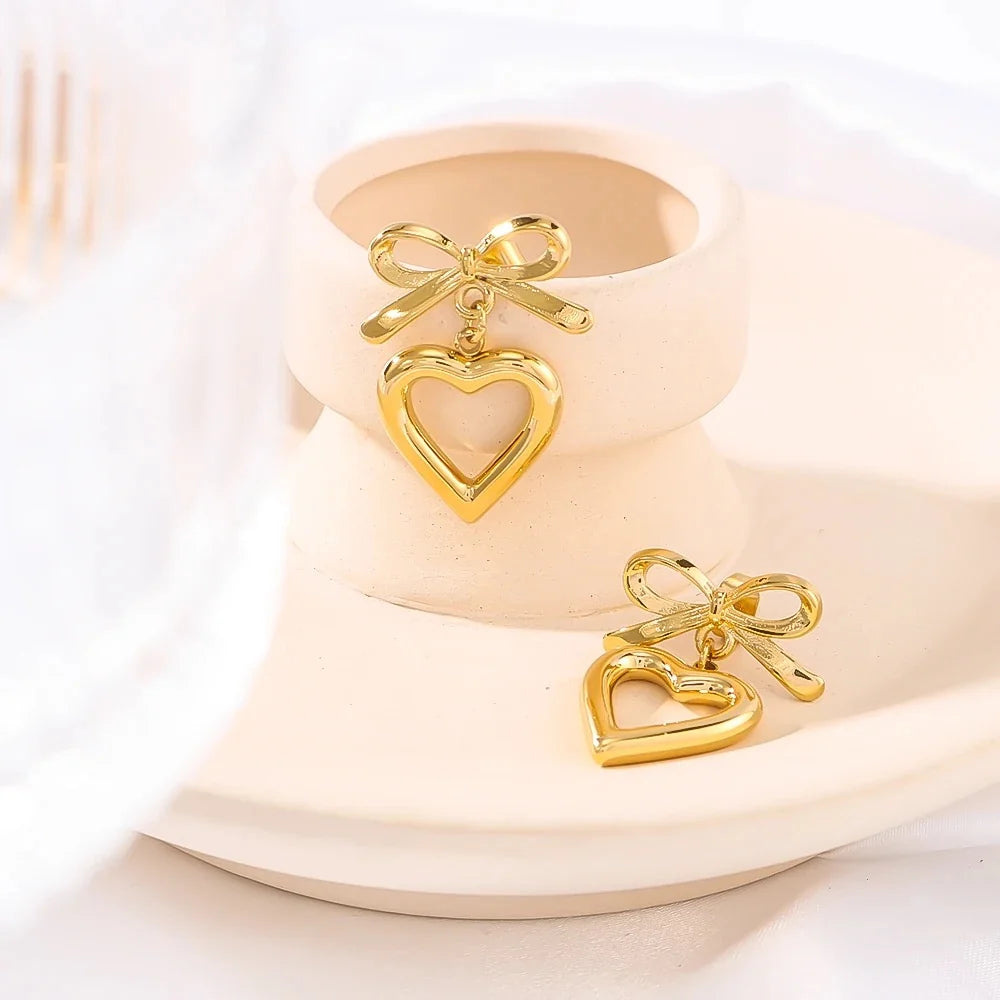 Gold bow and open heart drop earrings on white ceramic bowl