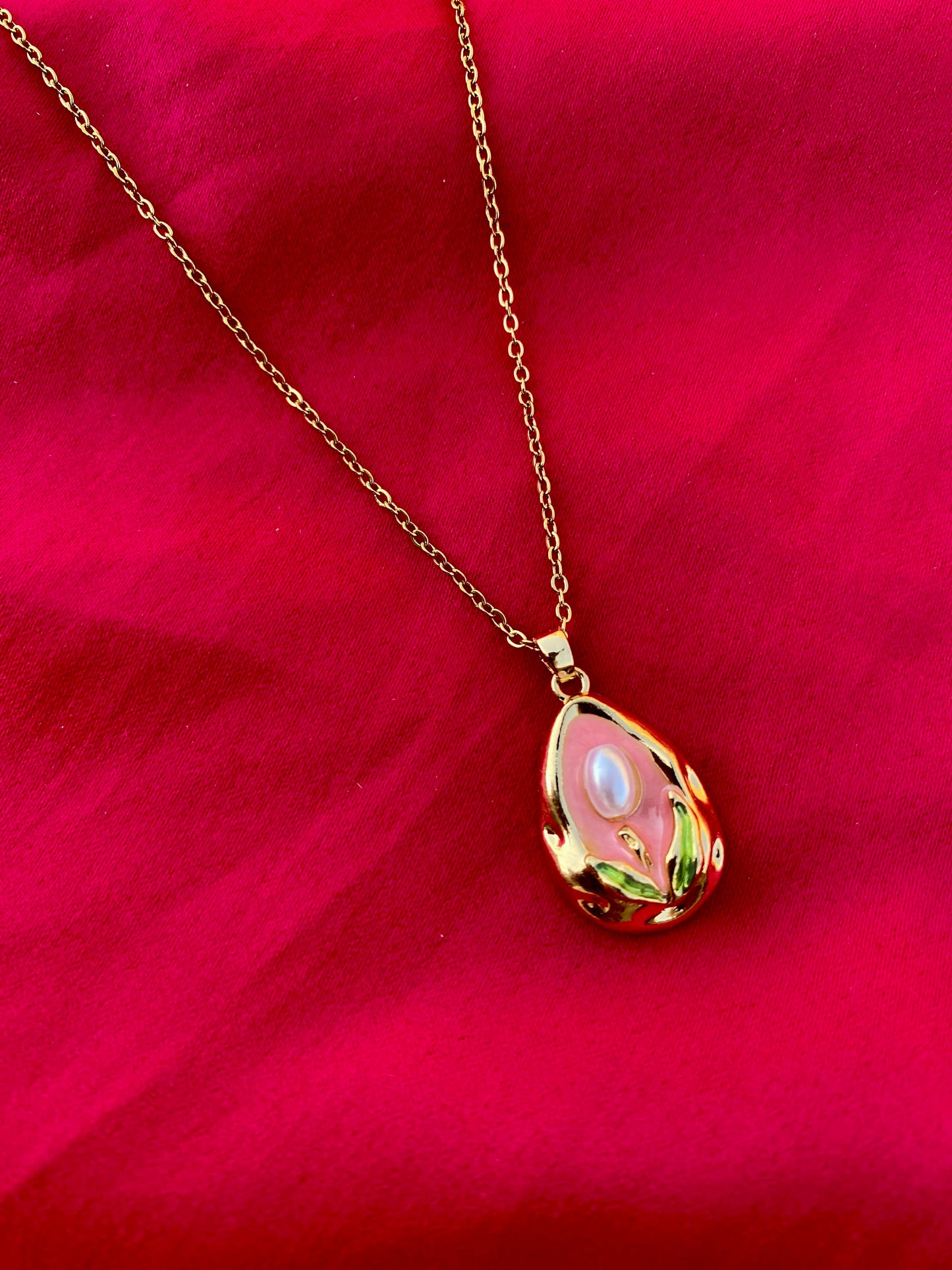 Modern Gold Drop Necklace with Pearl Detail on a Pink Background