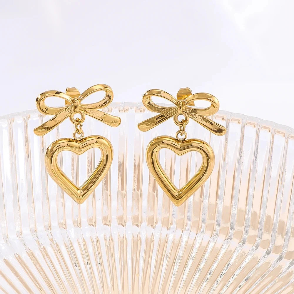 Gold bow open heart drop earrings on glass crystal display