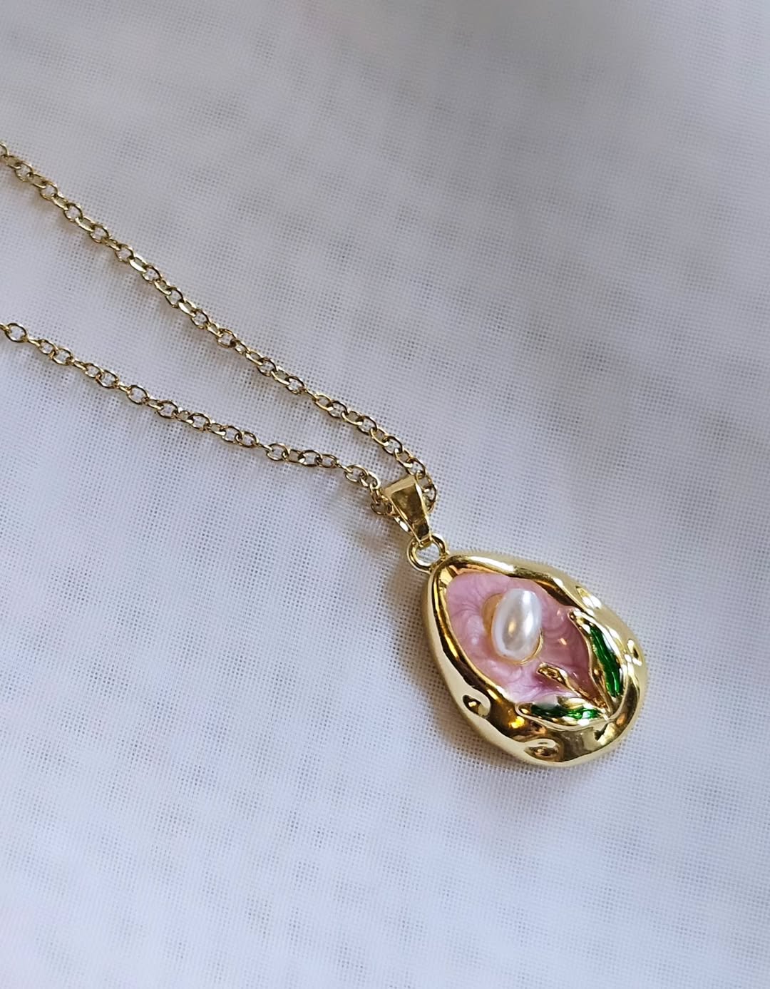 Modern Gold Drop Necklace with Pearl Detail on a Pink Background