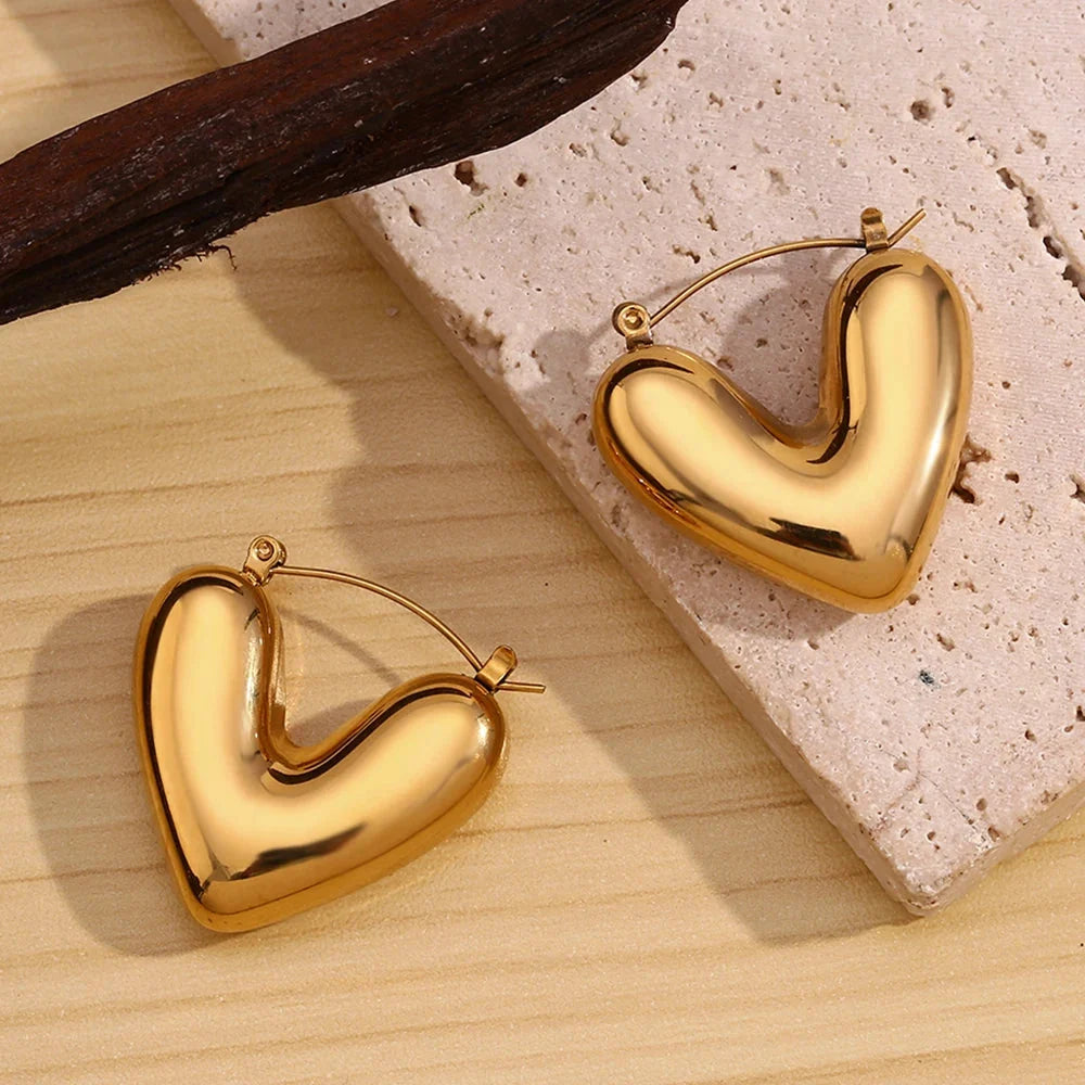 Chunky gold heart hoop earrings on stone surface