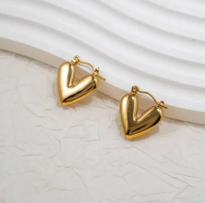 Pair of chunky gold heart hoop earrings on white surface