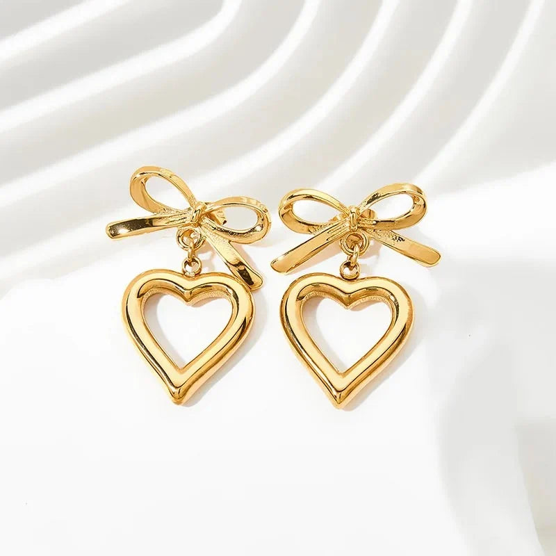 Pair of gold bow and open heart drop earrings on white silk background