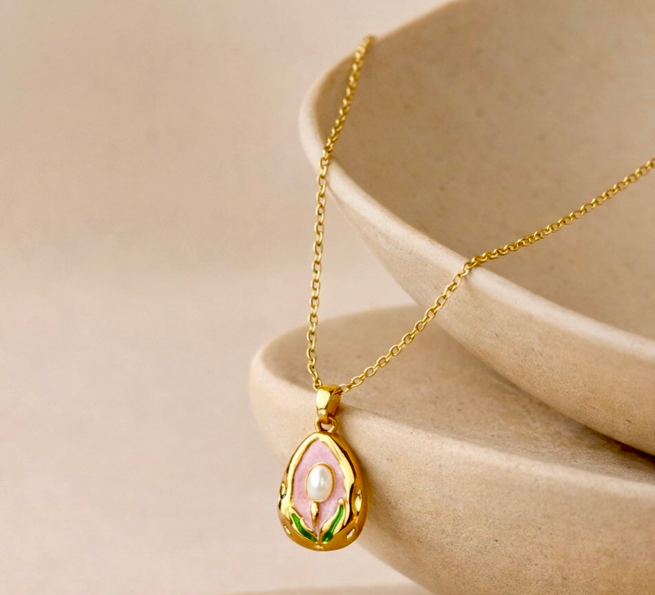 Modern Gold Drop Necklace with Pearl Detail on a Pink Background