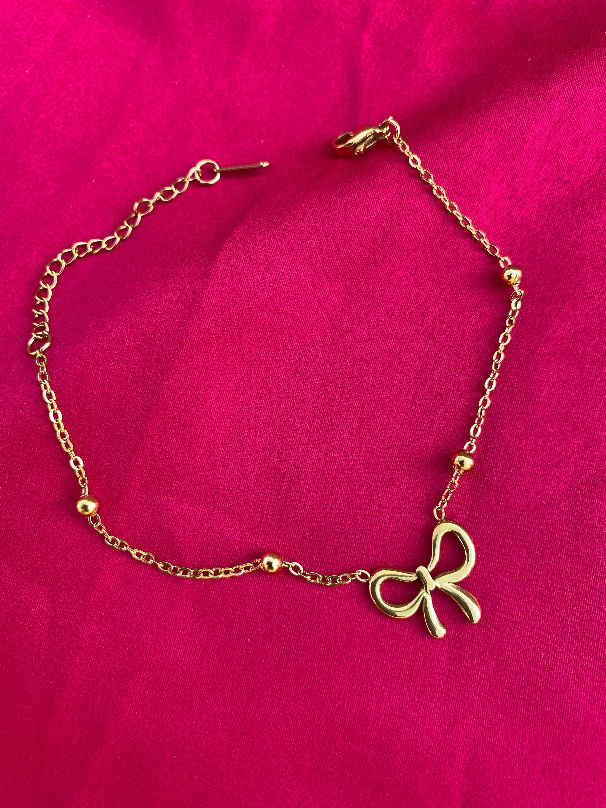 Gold bracelet with a bow charm on a pink background