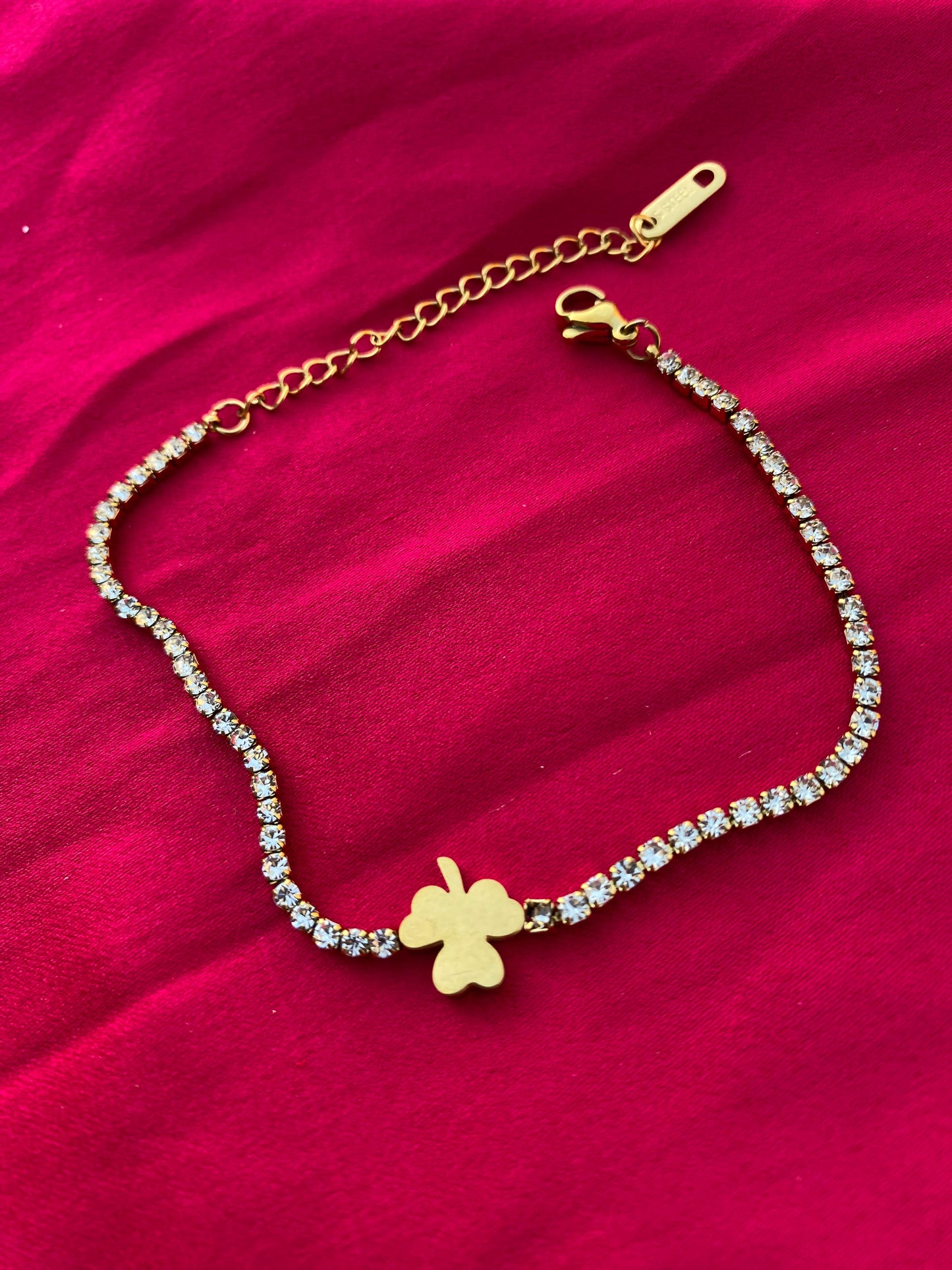 Gold bracelet with a clover charm on a red fabric background