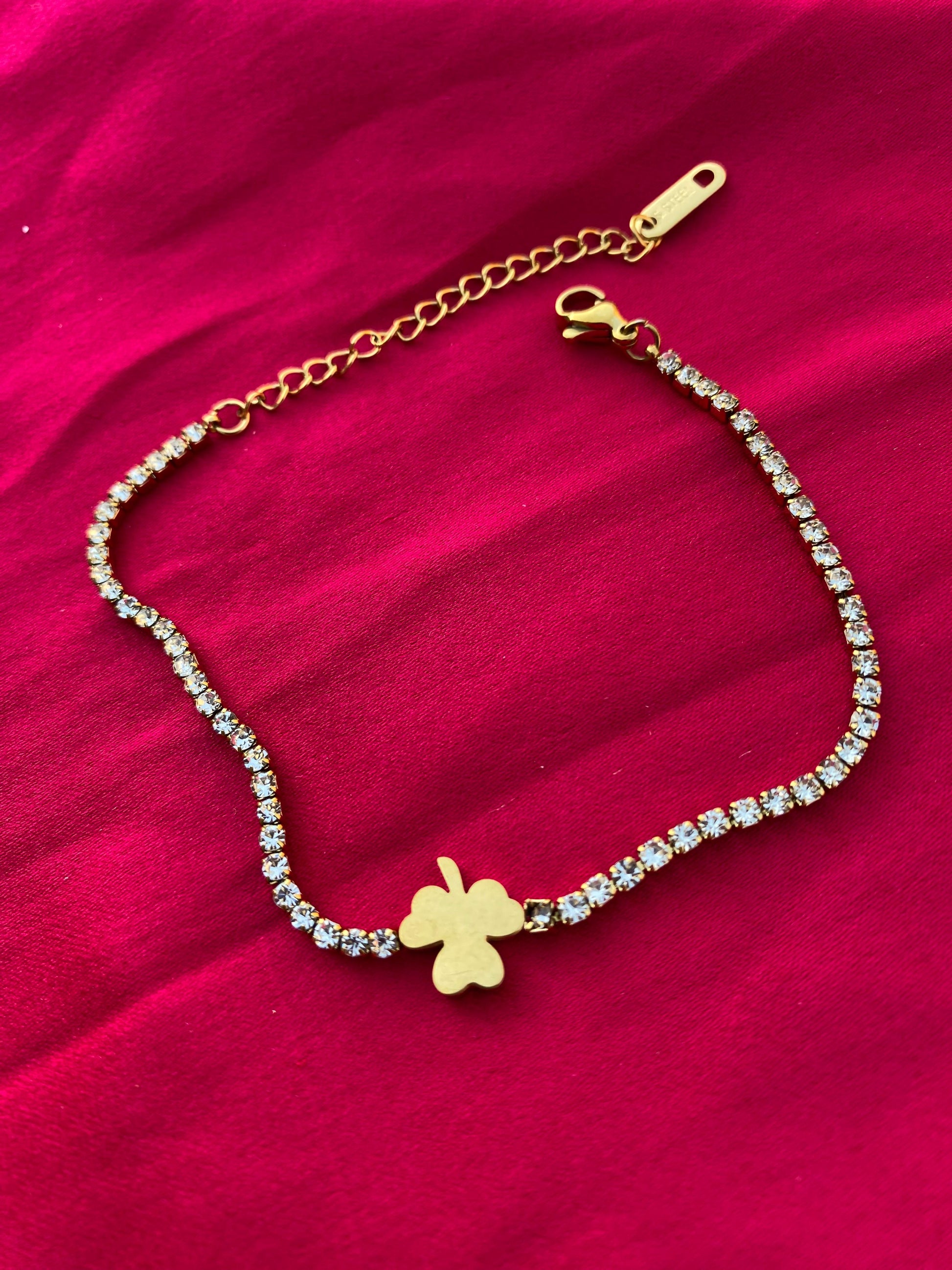 Gold bracelet with a clover charm on a red fabric background