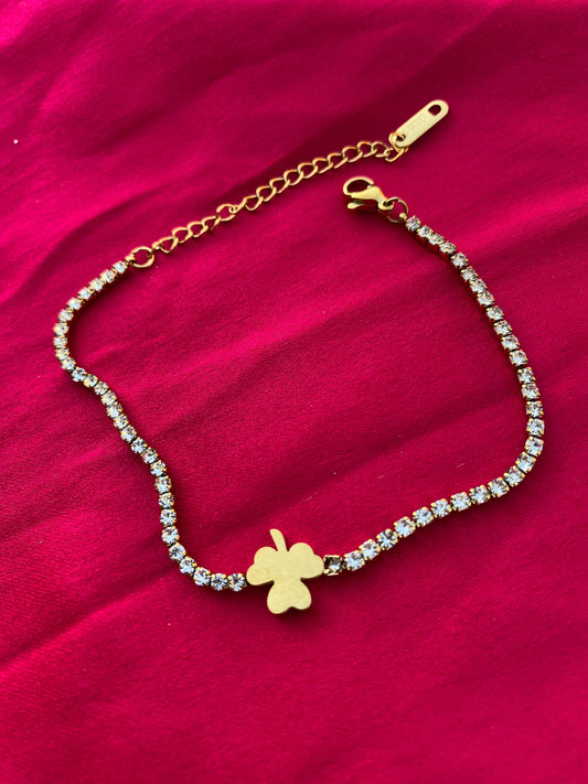 Gold bracelet with a clover charm on a red fabric background