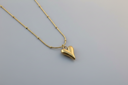 Gold heart-shaped pendant necklace on a marble surface with a pink fabric background