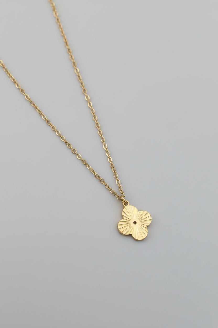 Gold necklace with a floral pendant on a stone surface with a red fabric background