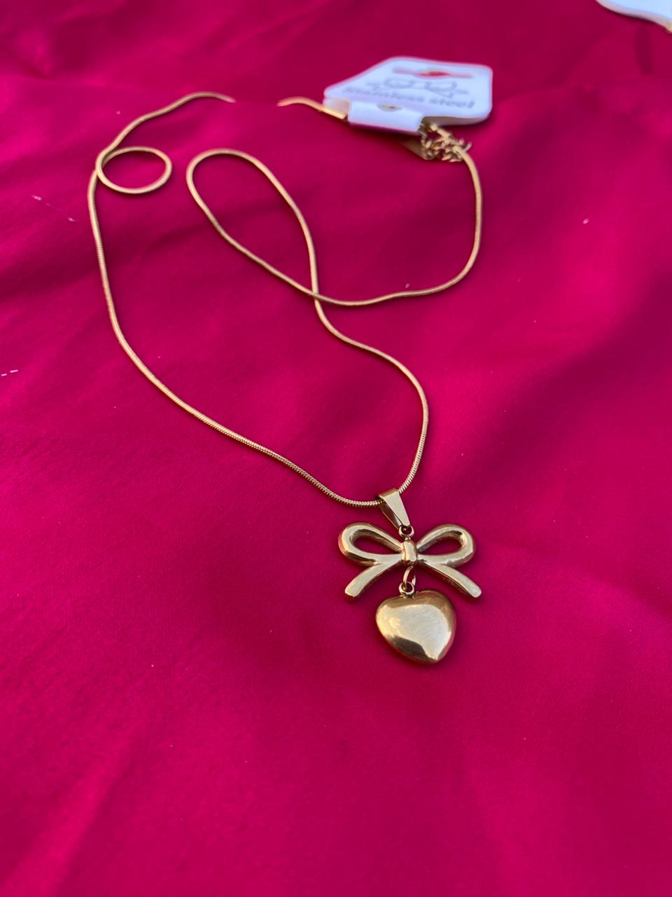 Gold necklace with a heart-shaped pendant on a pink fabric background
