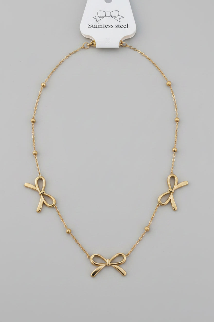 Gold necklace with bow-shaped pendants on a pink background