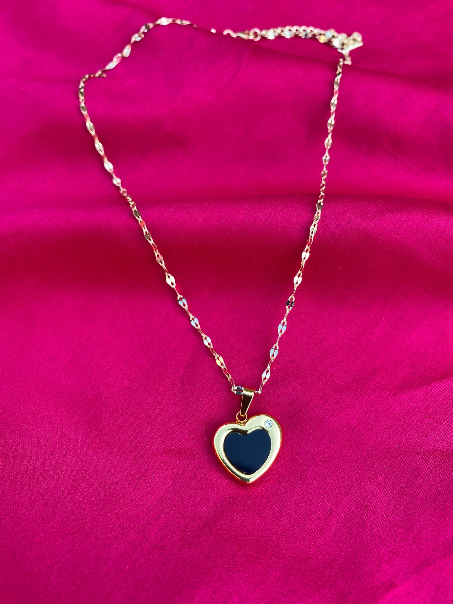 Necklace with a heart-shaped black pendant on a pink background