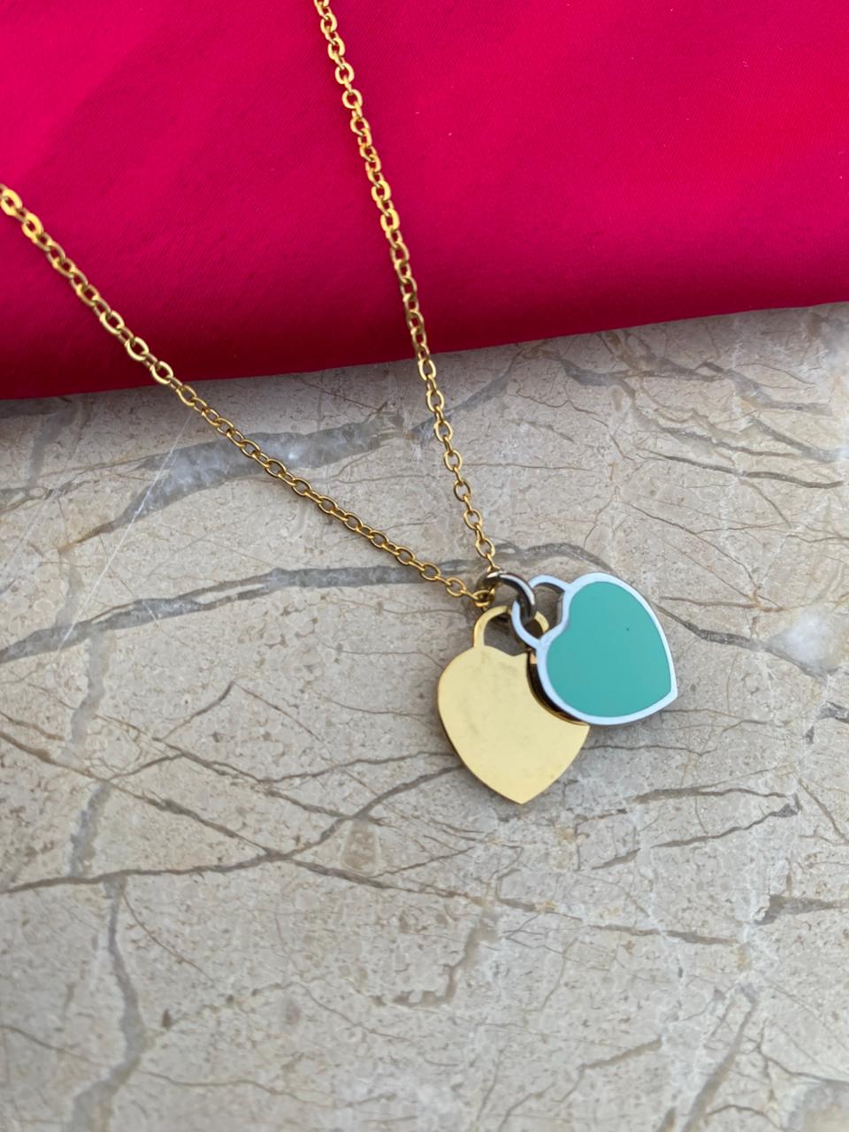 Necklace with gold and teal heart pendants on a textured surface with a red fabric background