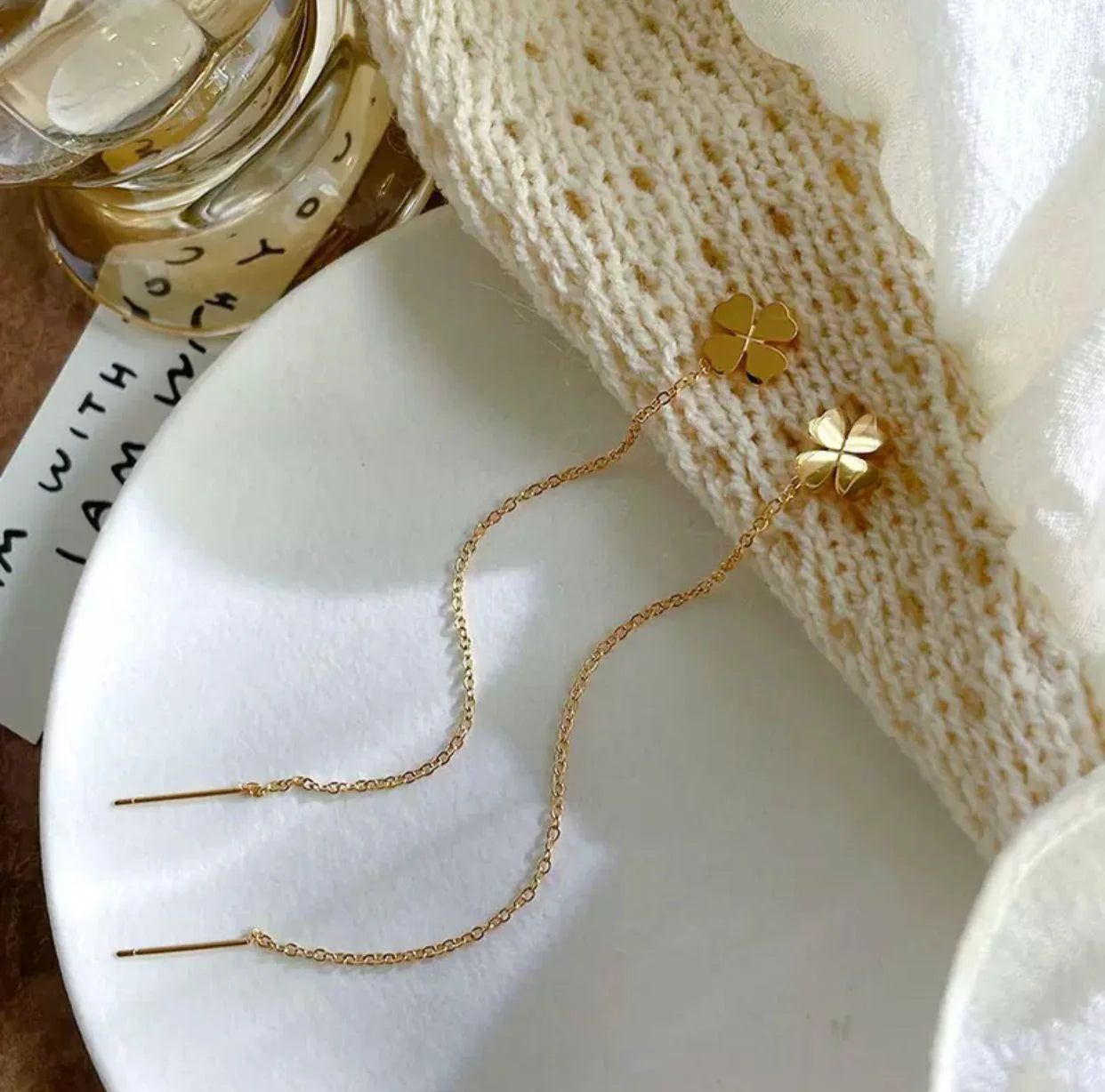 Pair of gold clover threader drop earrings on white plate