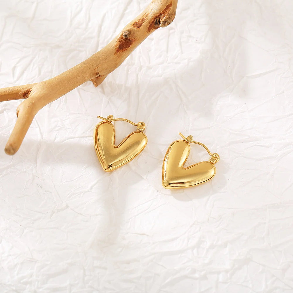 Chunky gold heart hoop earrings styled on white background with wood