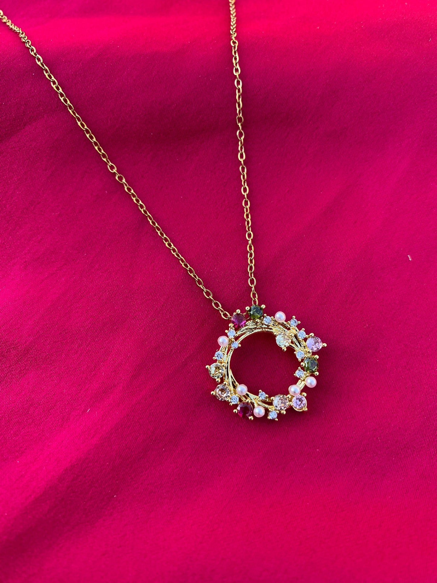 Necklace with a circular pendant featuring colorful stones on a pink background