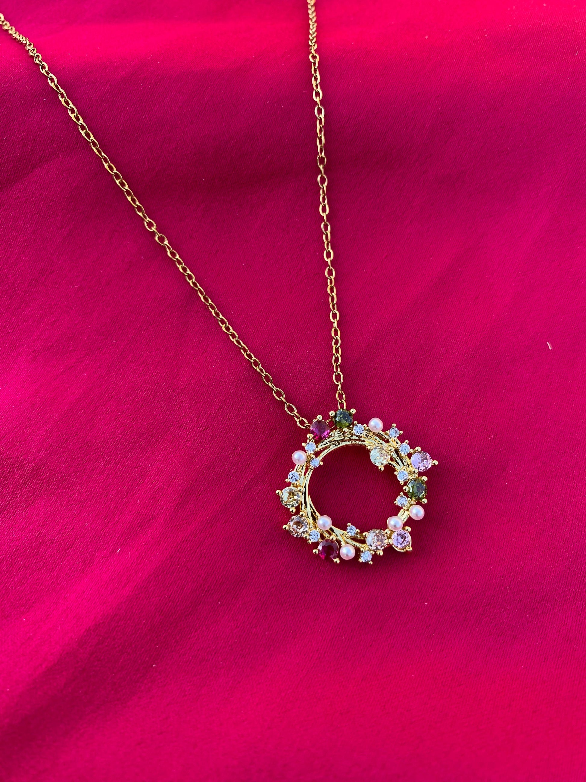 Necklace with a circular pendant featuring colorful stones on a pink background
