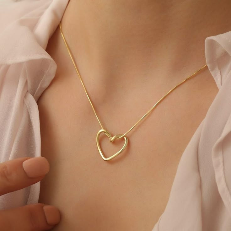 Gold heart-shaped necklace on a person wearing a light pink blouse.